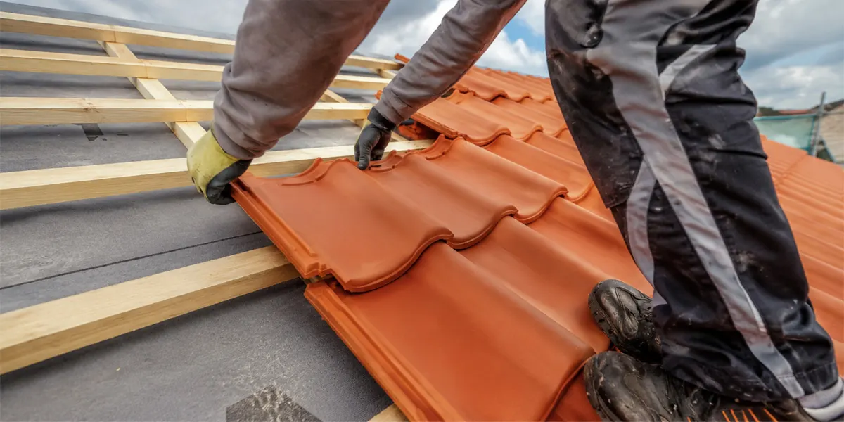 Couvreur posant des tuiles orange sur une toiture